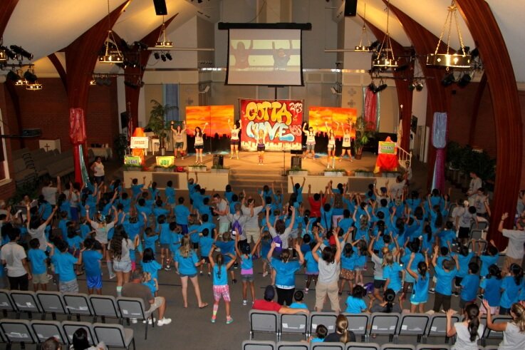 Overhead shot of children and adults in church raising up their hands.